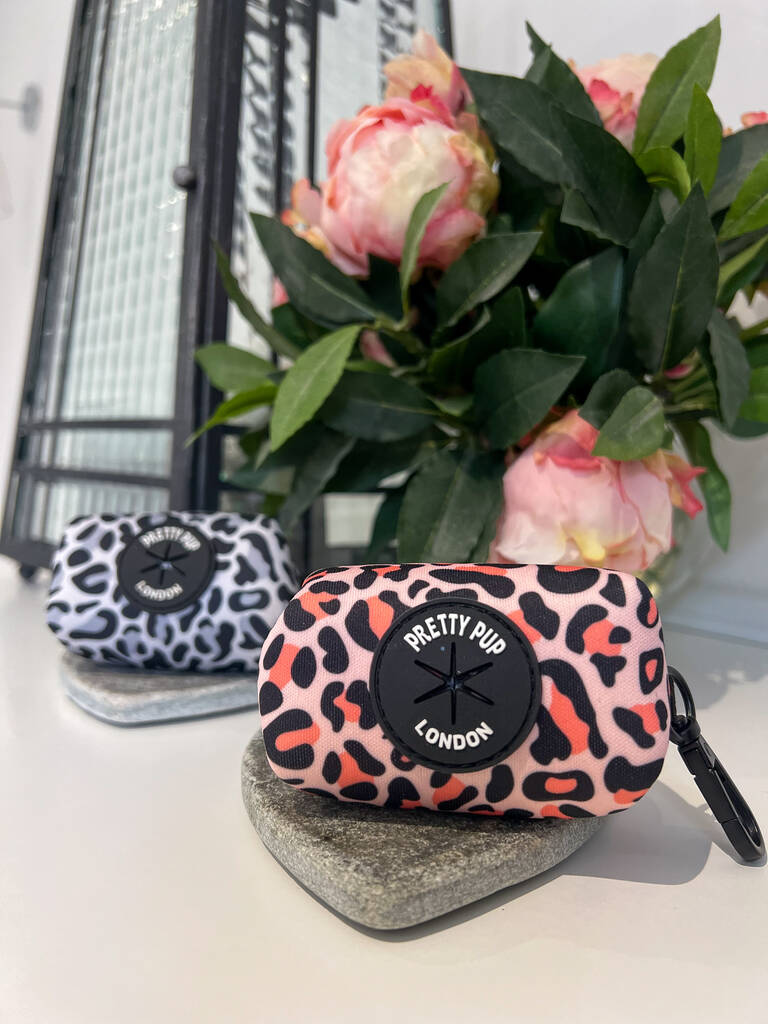 orange dog poo bag dispenser with matching grey dog poo bag dispenser both with leopard print pattern lay on a countertop